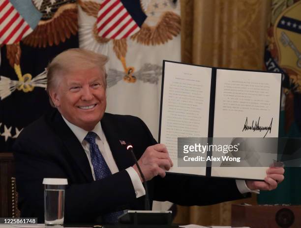 President Donald Trump holds up a copy of an executive order he signed on DOT deregulation, during a meeting with his cabinet in the East Room of the...