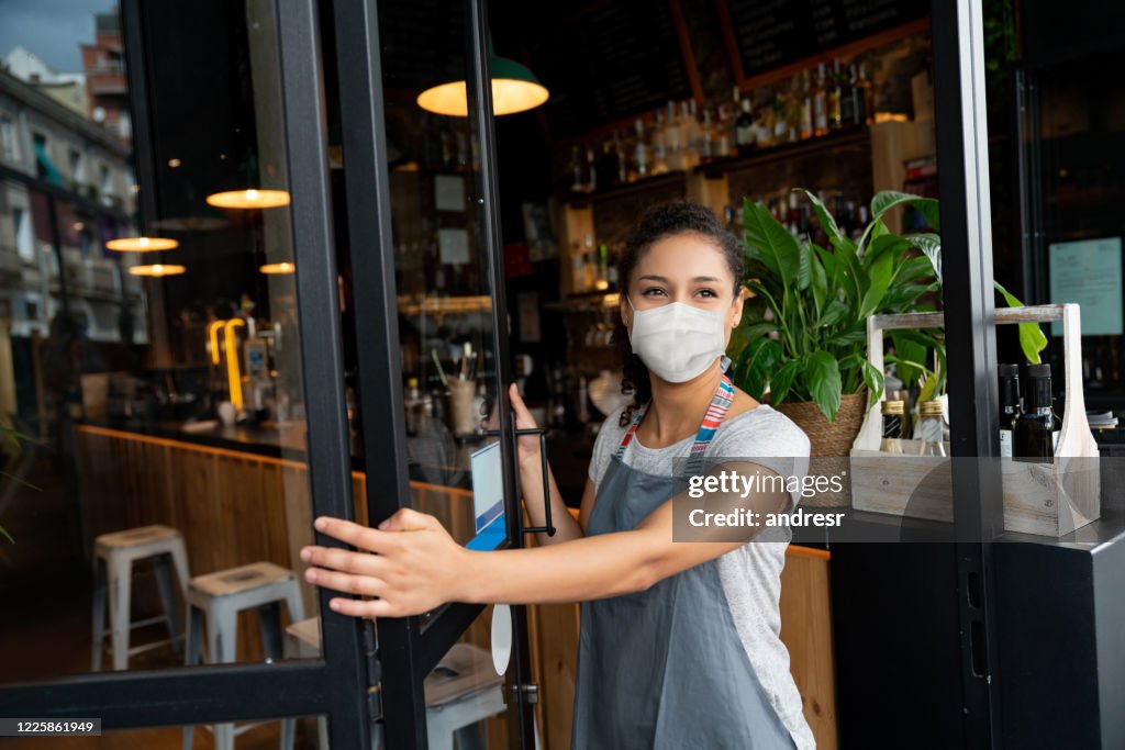 Propriétaire heureux d’affaires ouvrant la porte à un café utilisant un masque facial