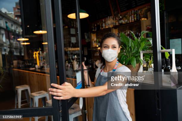 felice imprenditore che apre la porta in un bar indossando una maschera facciale - inaugurazione foto e immagini stock