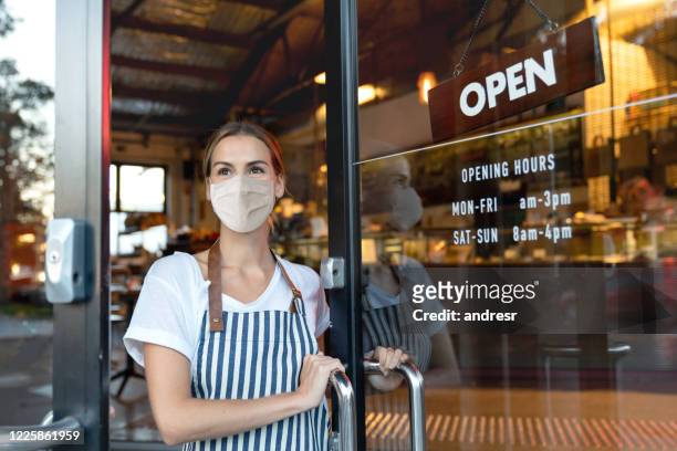 happy business owner opening the door at a cafe wearing a facemask - opening event stock pictures, royalty-free photos & images