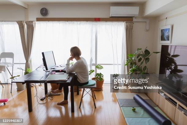 a woman using a computer in the living room of her home - telecommuting stock pictures, royalty-free photos & images