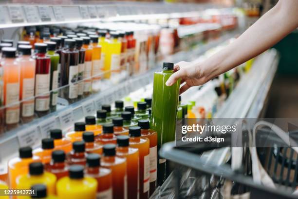 cropped shot of young asian woman shopping for fresh fruit juice from refrigerated shelves in supermarket and putting a bottle of fresh squeezed orange juice into cotton mesh eco bag in a shopping cart. zero waste concept - juice foto e immagini stock