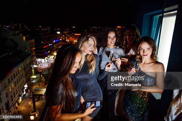 four women dressed to go out for the evening standing outside on a balcony with glasses of champagne. - slumber party - fotografias e filmes do acervo