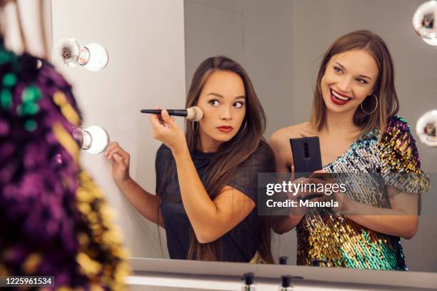 two women putting on make up and looking in a mirror. - friends women makeup stock pictures, royalty-free photos & images