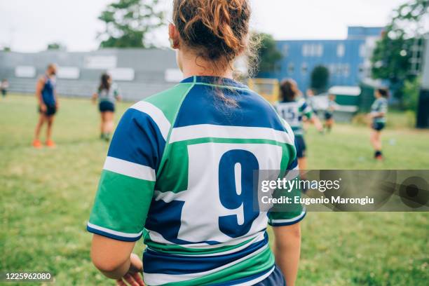 rear view of a woman wearing a blue, green and white rugby shirt on a pitch at training with other players in the background. - sports jersey back stock pictures, royalty-free photos & images