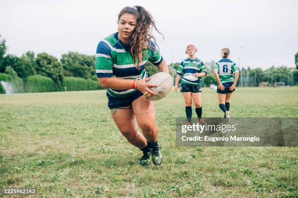 three women wearing blue, white and green rugby shirts on a training pitch, one running with a rugby ball. - rugby boot stock pictures, royalty-free photos & images