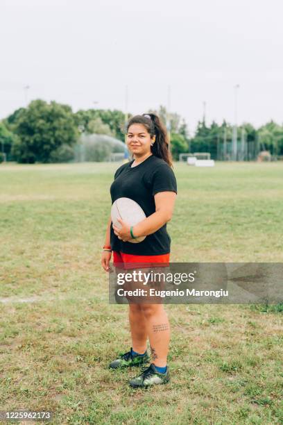 a woman standing on a training pitch in shorts and tee shirt holding a rugby ball. - rugby boot stock pictures, royalty-free photos & images