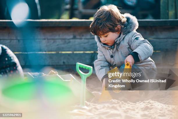 a child in a sandpit with a toy digger and spade. - sandkasten stock-fotos und bilder