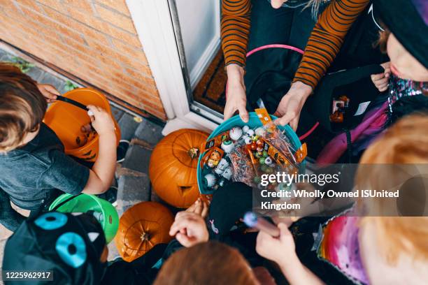 overhead view  of a group of children at a front door taking sweets from a bowl at halloween. - halloween party - fotografias e filmes do acervo