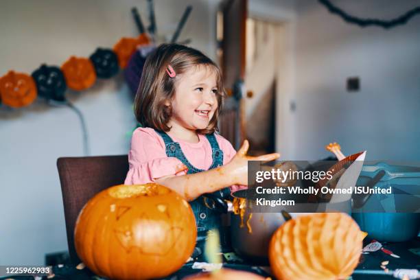 a smiling girl taking the pumpkin seeds and flesh from her fingers. - fruit flesh stock pictures, royalty-free photos & images