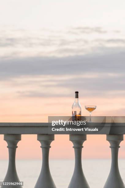 bottle of rose wine and beautiful wine glass on the white columns on sunset seascape view background - ballustrade stockfoto's en -beelden