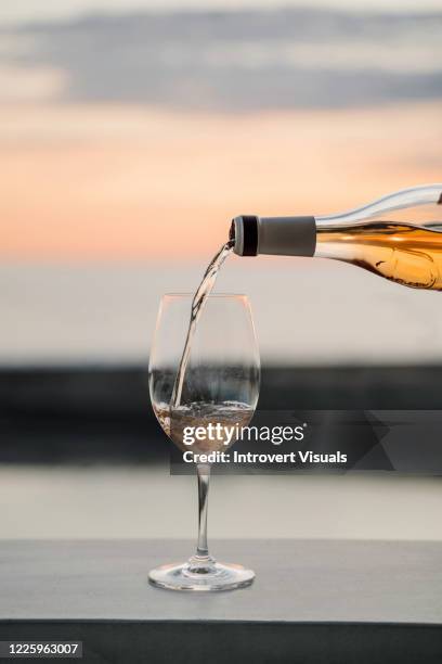 wine is pouring from the bottle into the glass with sunset sea view on the background - glass half full party stock pictures, royalty-free photos & images