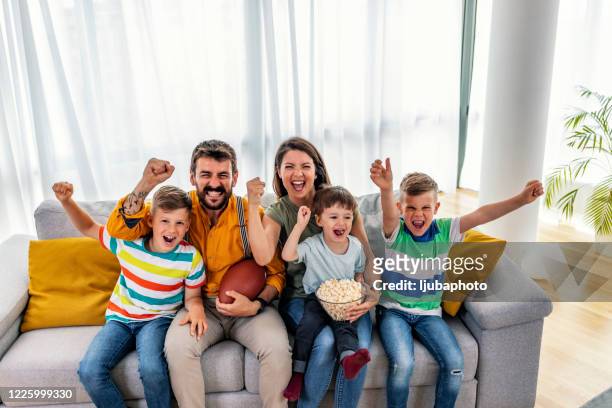 cheerful family cheering while watching rugby match on tv at home - american football family stock pictures, royalty-free photos & images