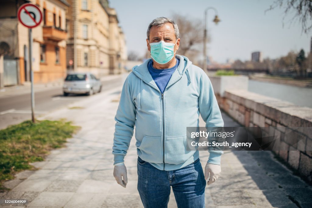 Uomo anziano con maschera protettiva che cammina per strada in città