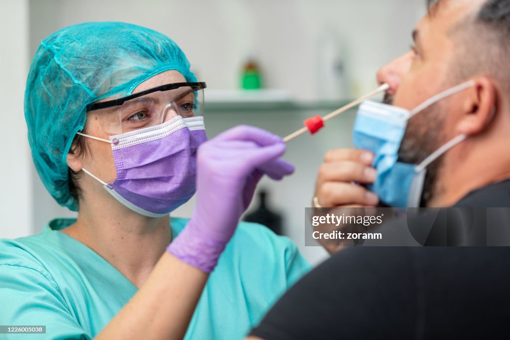 Female doctor in protective workwear taking nose swab test from mid adult man