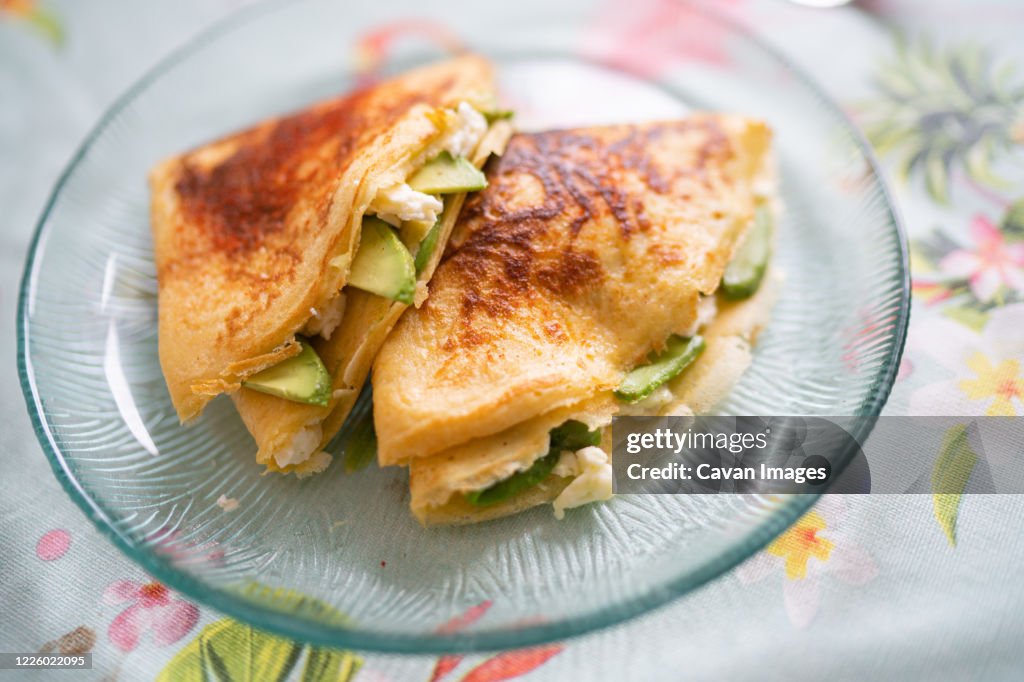 A plate of pancakes with cheese and avocado is on the table with a colorful tablecloth