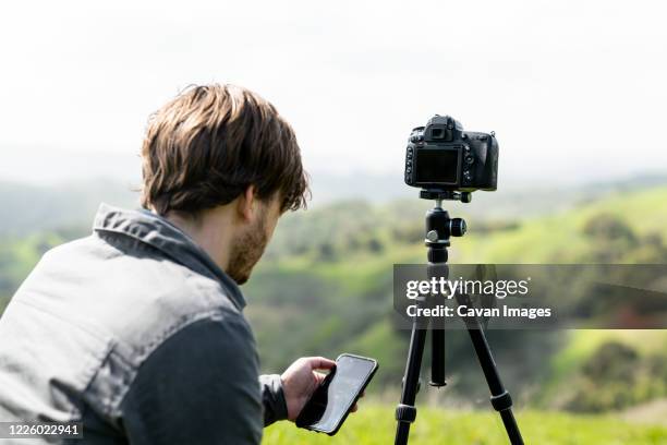 person using smartphone app to control camera on tripod outdoors - tripod stock-fotos und bilder