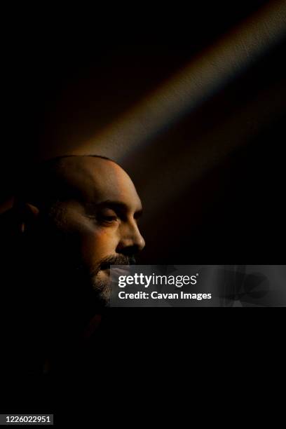 man sitting in a rainbow beam along a dark wall in basement - portrait professional dark background stock-fotos und bilder