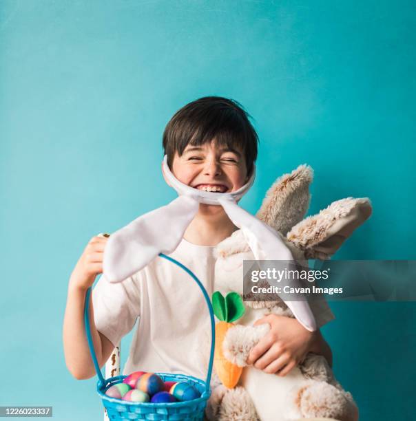 boy wearing bunny ears holding toy rabbit and easter eggs in a basket. - easter basket - fotografias e filmes do acervo