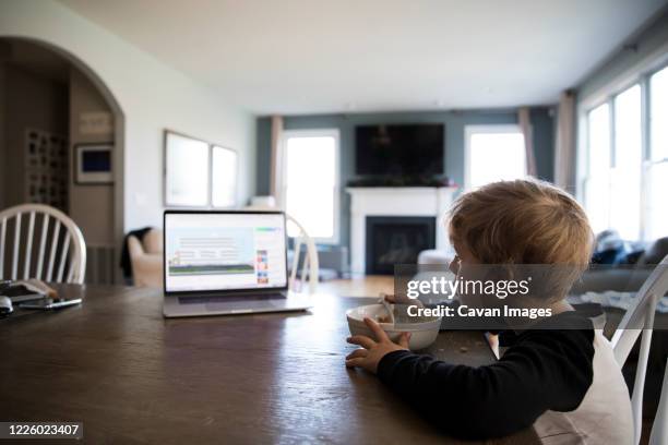 wide side view of blonde boy eating cereal watching lesson on laptop - child eat side photos et images de collection