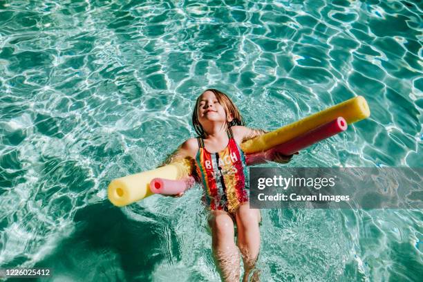 young girl swimming on her back in pool with eyes closes - cavan images stock-fotos und bilder