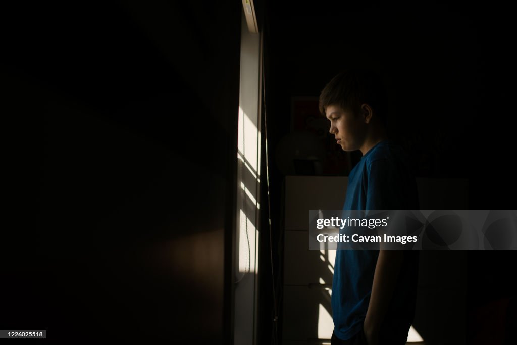 Young teen boy looking out the window during isolation