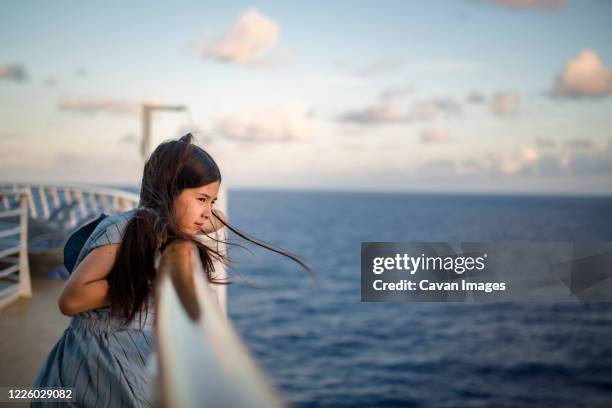 a young girl leans against a ship railing at sunset gazing at ocean - cruise ship stock-fotos und bilder