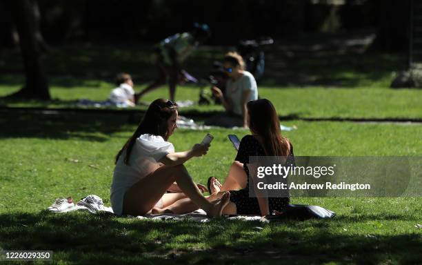Two women are on their phones while sunbathing on May 20, 2020 in the Putney area of London, England. The British government has started easing the...