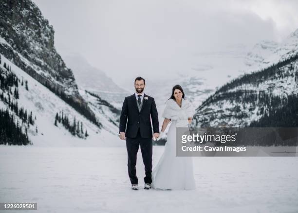 newlywed couple stand on frozen lake louise, alberta canada in winter - winter wedding stock pictures, royalty-free photos & images