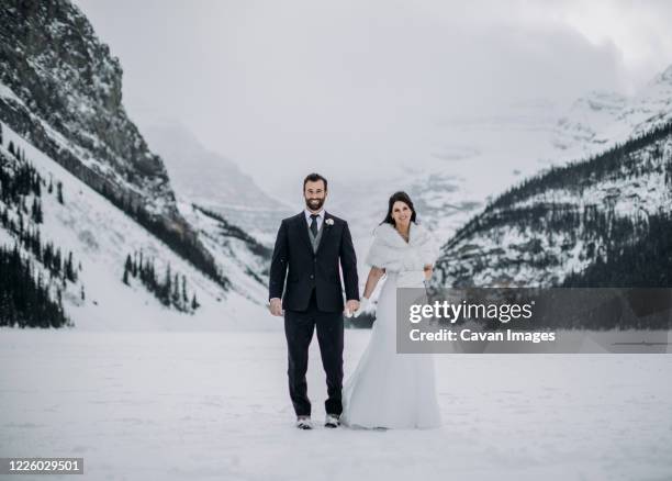 newlywed couple stand on frozen lake louise, alberta canada in winter - banff wedding stock pictures, royalty-free photos & images
