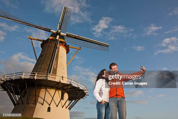 mature couple taking selfie with windmill in the netherlands - middelburg netherlands stock-fotos und bilder