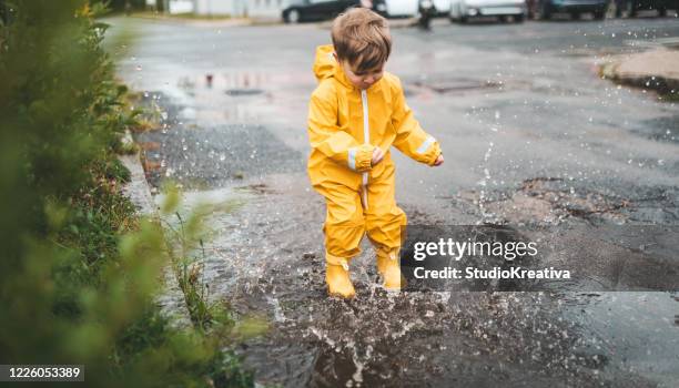 小さな男の子は雨の中で遊んで、水の塗料に飛び込む - puddle ストックフォトと画像