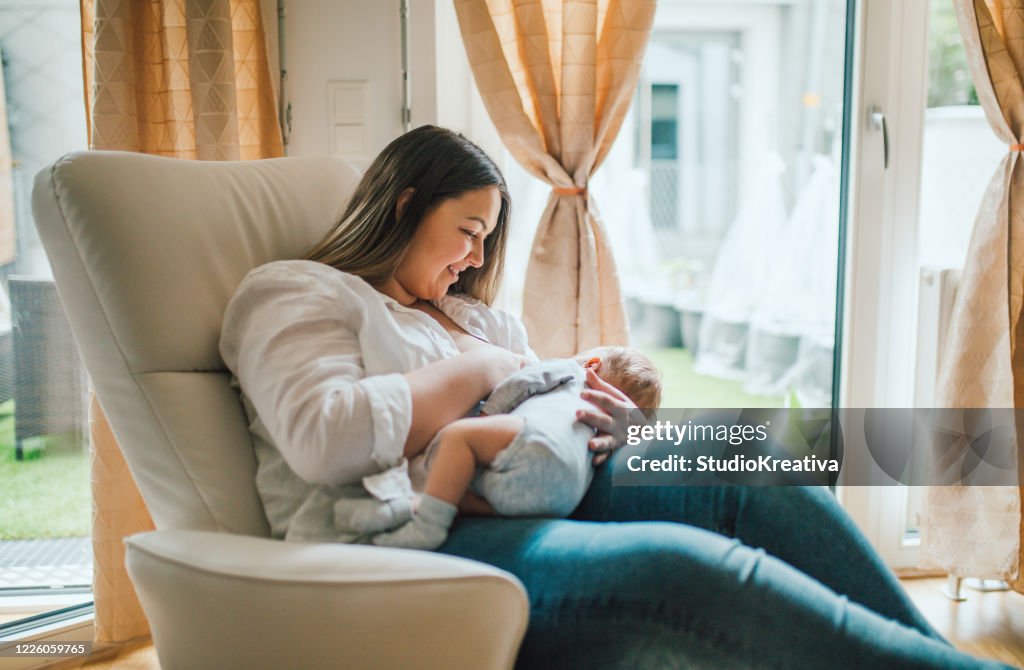 Mother breastfeeds and plays with her newborn baby