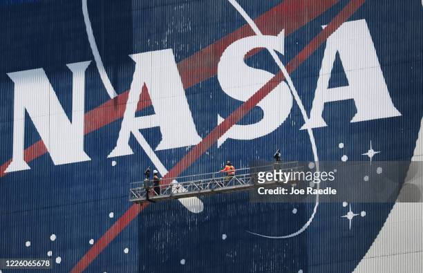 Workers freshen up the paint on the NASA logo on the Vehicle Assembly Building before the arrival of NASA astronauts Bob Behnken and Doug Hurley at...