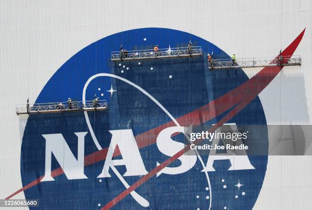 Workers freshen up the paint on the NASA logo on the Vehicle Assembly Building before the arrival of NASA astronauts Bob Behnken and Doug Hurley at...