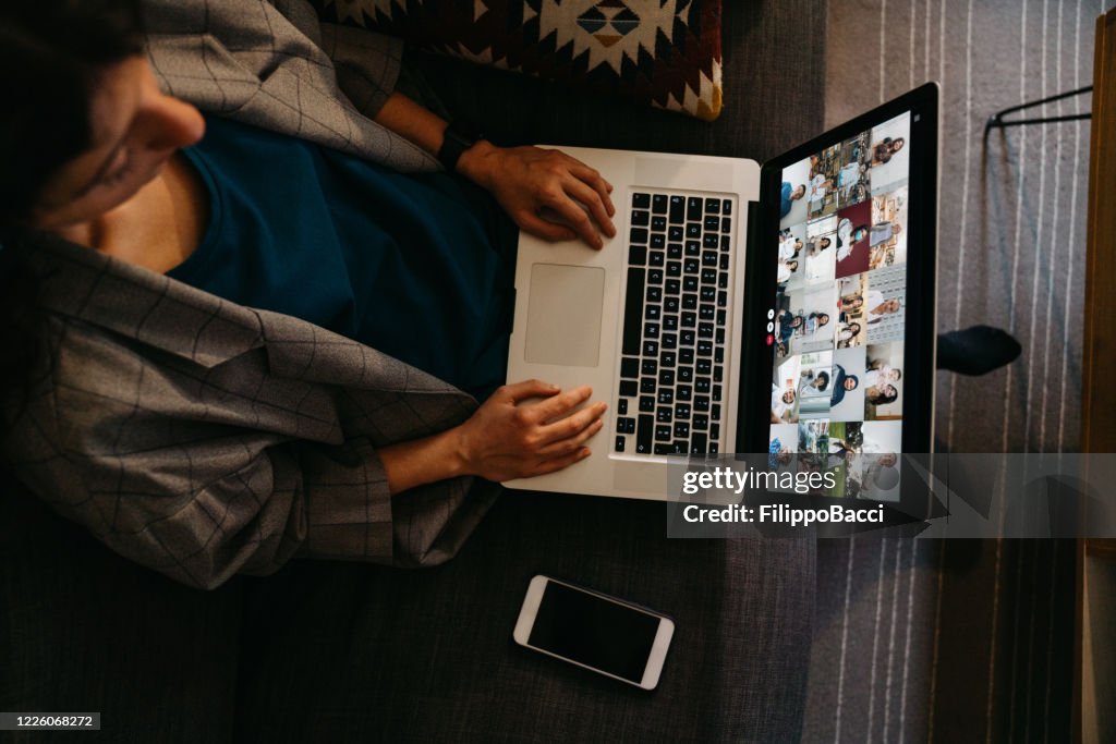 Junge Frau mit einem Laptop auf dem Sofa zu Hause, um eine Arbeitskonferenz zu haben