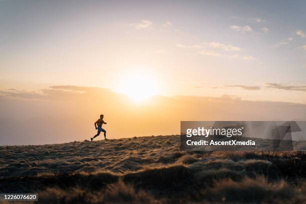 young man trail runs up mountain at sunrise - forward athlete stock pictures, royalty-free photos & images