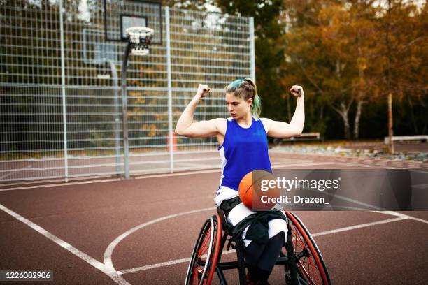 muscular woman in wheelchair showing biceps muscles with basketball ball in her lap - disability sport and recreation - teenager cerebral palsy stock pictures, royalty-free photos & images