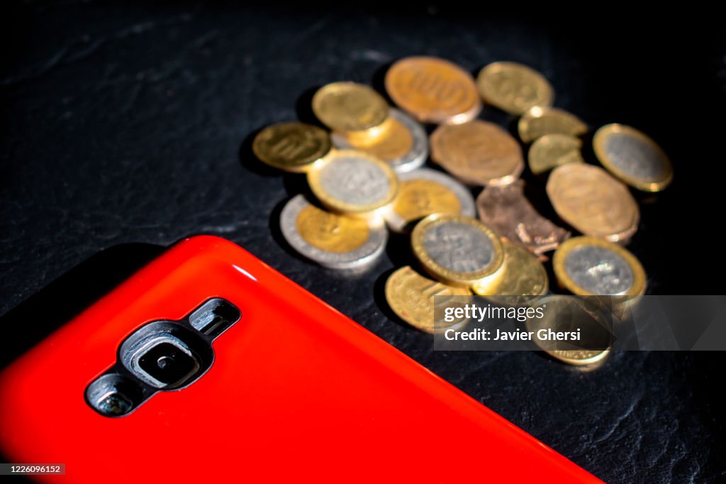 Dinero en efectivo: pesos chilenos en monedas y teléfono celular/móvil con protector rojo