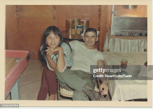 Young serviceman leans back in a chair and looks towards the camera, while dangling a cigarette from one hand and wrapping his other arm around a...