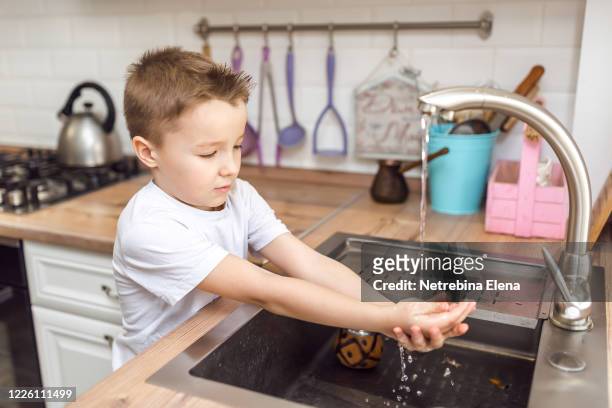 a boy in a white t-shirt washes his hands under the tap. a stream of water pours on the palms of your hands. hand hygiene is the key to health - stream body of water fotografías e imágenes de stock