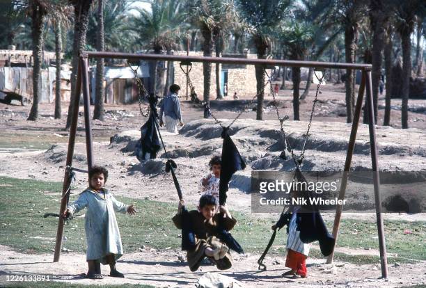Iraqi children in scruffy robes play on swing set where broken swings have been replaced by black pieces of clothcirca 1978 ,