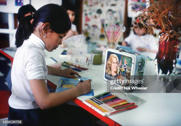 Primary school girl draws at her desk in front of her lunch pail with picture of Bionic Woman at private school in Baghdad, circa 1978