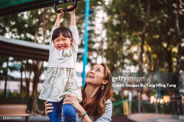 young asian mom supporting her little daughter while playing with the climbing rings in outdoor playground joyfully - monkey bars stock pictures, royalty-free photos & images