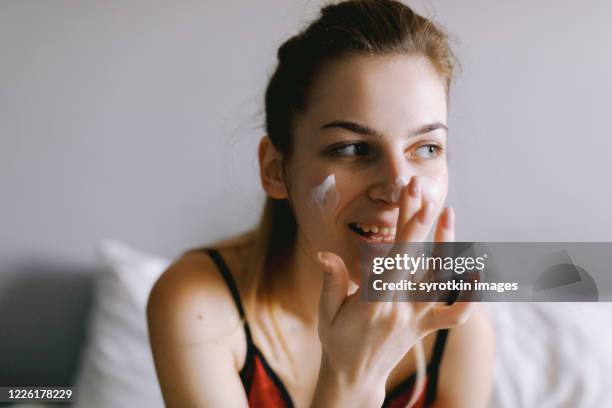 smiling woman applying cream on face - applying cream stock pictures, royalty-free photos & images