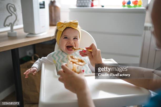 blij babymeisje dat lepel-gevoed door haar mamma krijgt - spoon feeding stockfoto's en -beelden