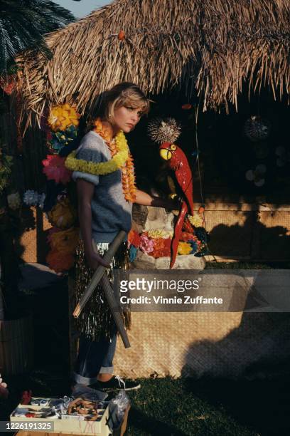 American actress Michelle Pfeiffer wearing leis over a grey sweatshirt, with a gold-coloured grass skirt over a pair of jeans, holding a model of a...