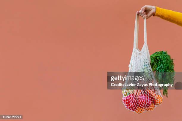 woman holding reusable cotton mesh bag with fruit and vegetables - tragetasche oder tragebeutel stock-fotos und bilder