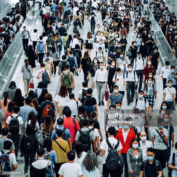 crowd of busy commuters with protective face mask walking through platforms at subway station during office peak hours in the city - commuter mask stock pictures, royalty-free photos & images