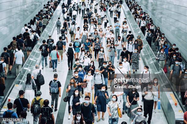 crowd of busy commuters with protective face mask walking through platforms at subway station during office peak hours in the city - hauptverkehrszeit stock-fotos und bilder